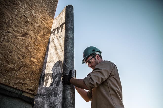 Construction worker installs housewrap to home