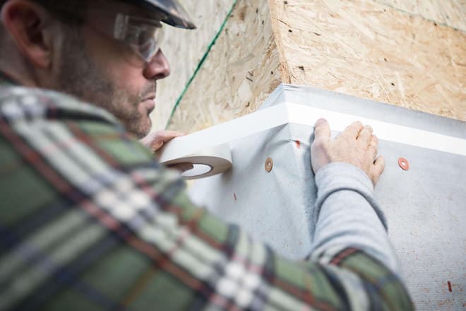 Man install housewrap using double sided seaming tape